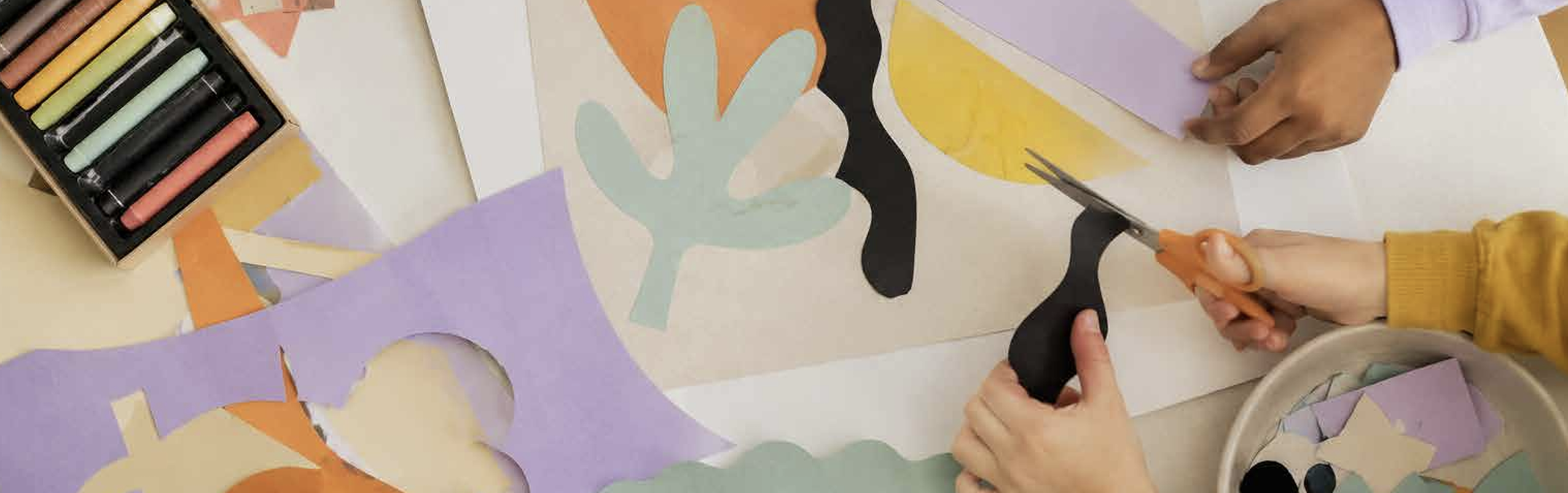 Manos recortando formas de papel de colores sobre una mesa con tizas pastel